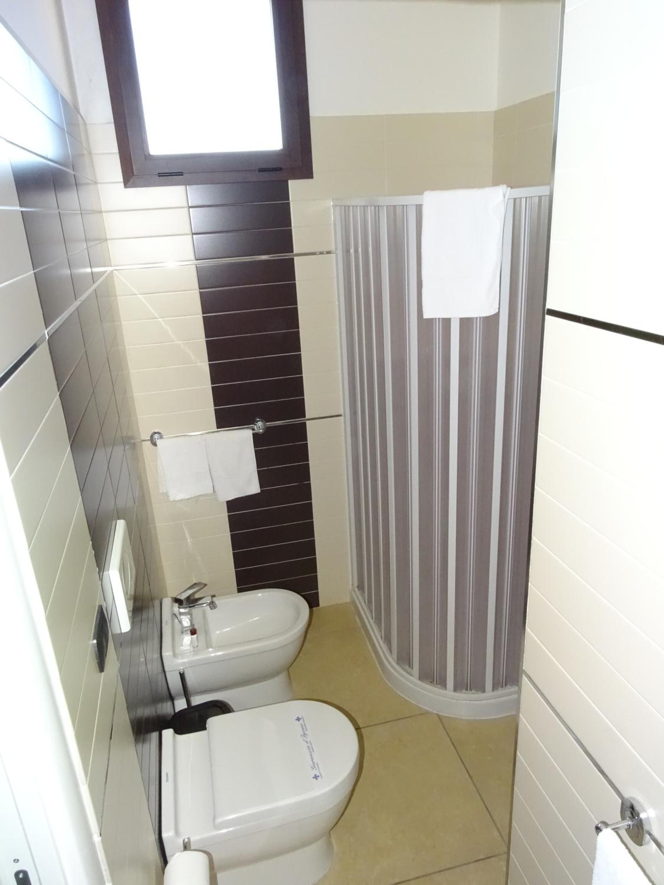 Een kleine badkamer met toilet, bidet en douche met een gestreepte gordijn.