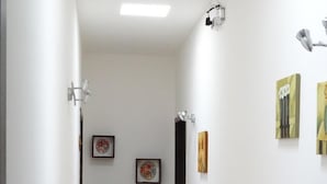 A narrow hallway with white walls and a tiled floor. There are three framed pictures on the wall, a door at the end, and a light fixture on the ceiling. - B&B Soleluna (Veglie)