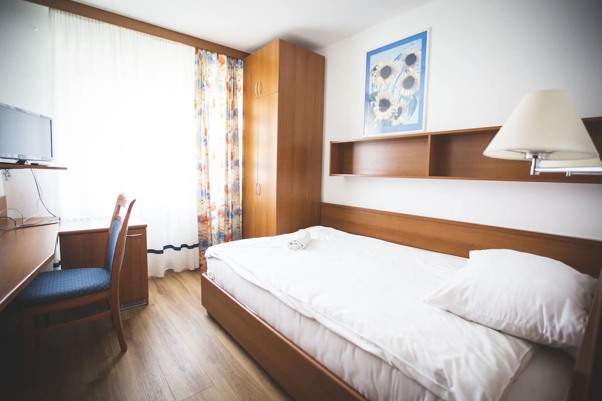 A hotel room with a wooden bed, a desk with a chair, a television, and a painting on the wall.