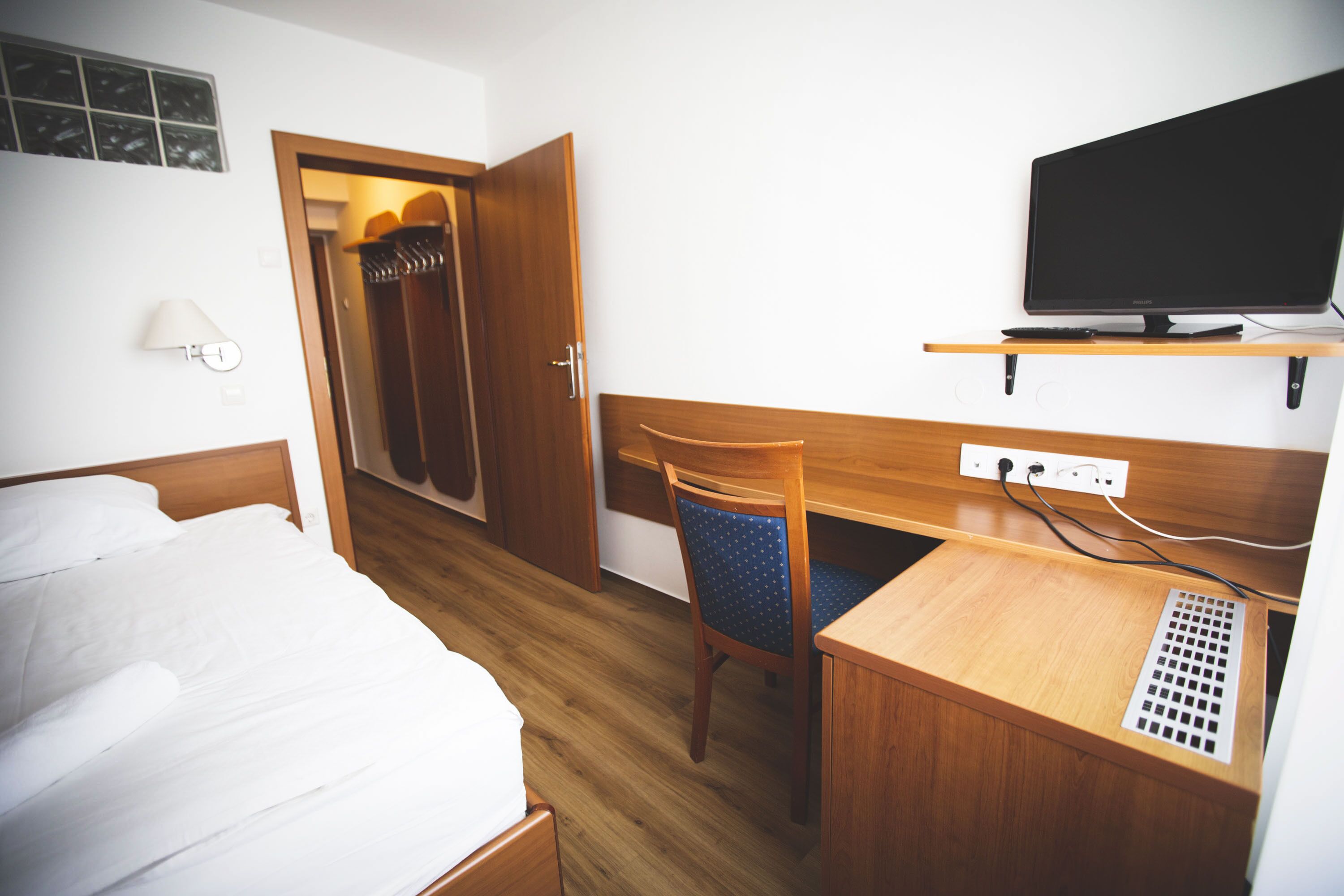 Una habitación de hotel con cama, escritorio, silla, televisión y armario.