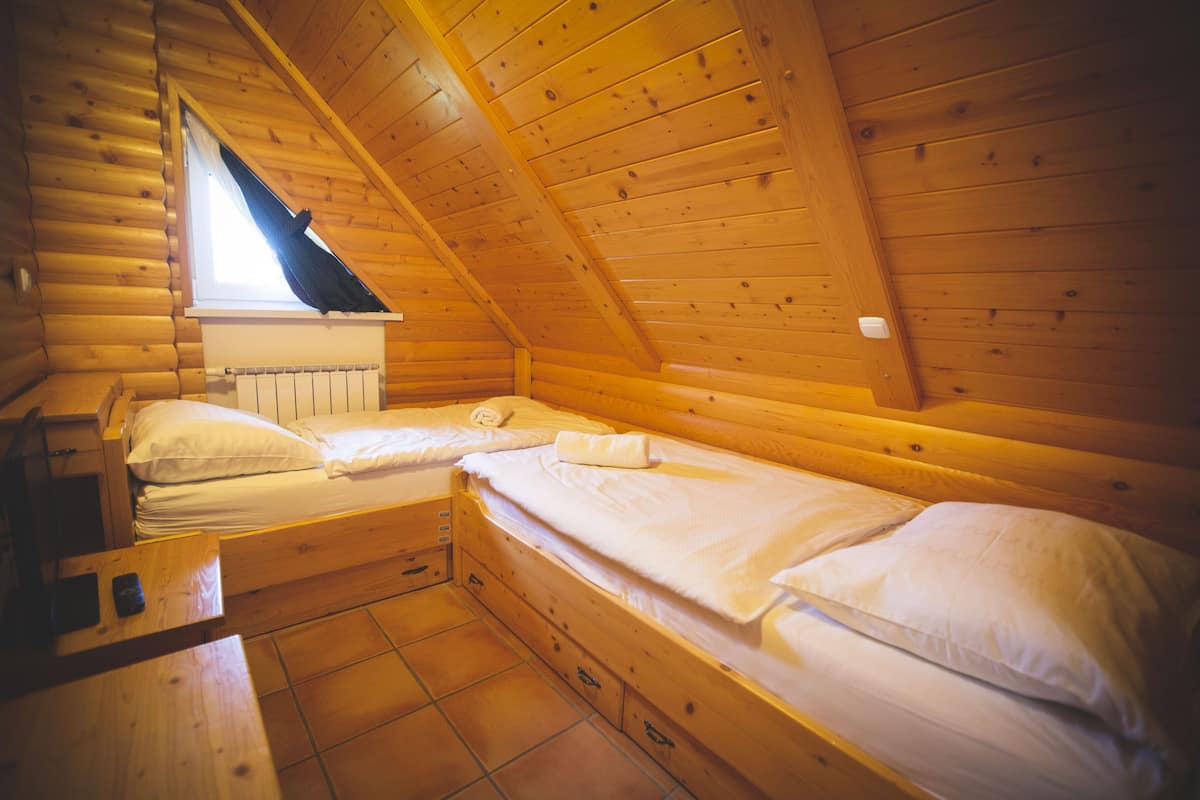 A cabin with two wooden bunk beds, a window with a black curtain, and a wooden table.