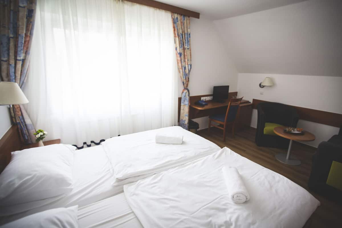 A hotel room with a bed, a desk, a chair, a lamp, and a small table.