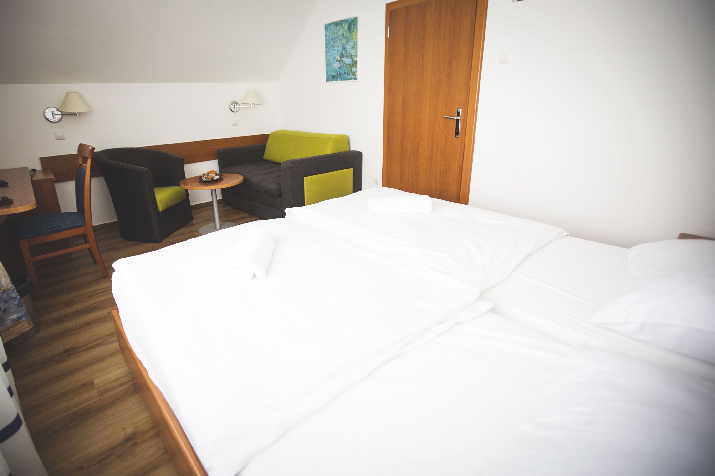 A hotel room with a large bed, a wooden floor, a desk, a chair, and a sofa with cushions.