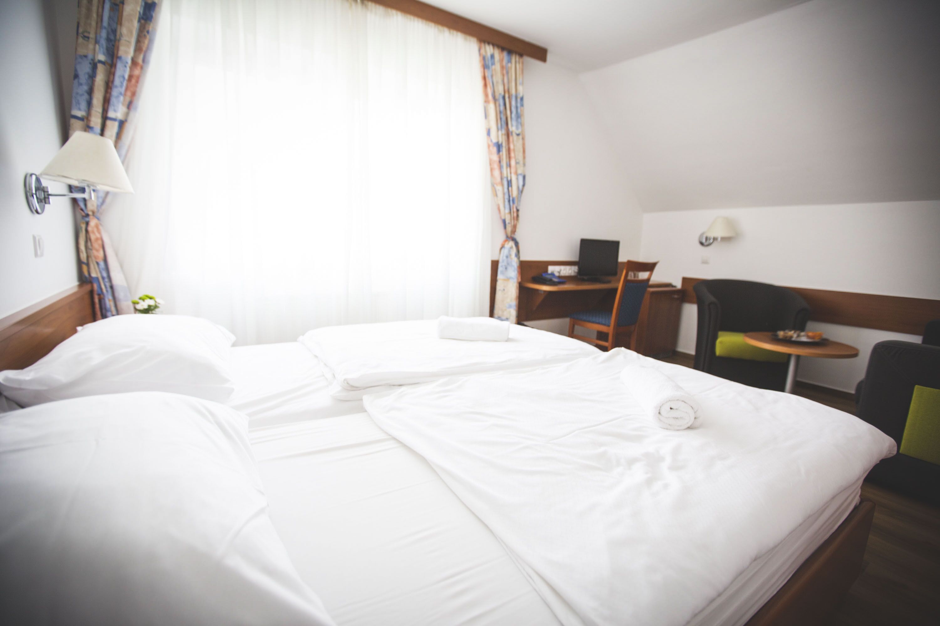A hotel room with two beds, a desk with a laptop, a chair, and a small table.