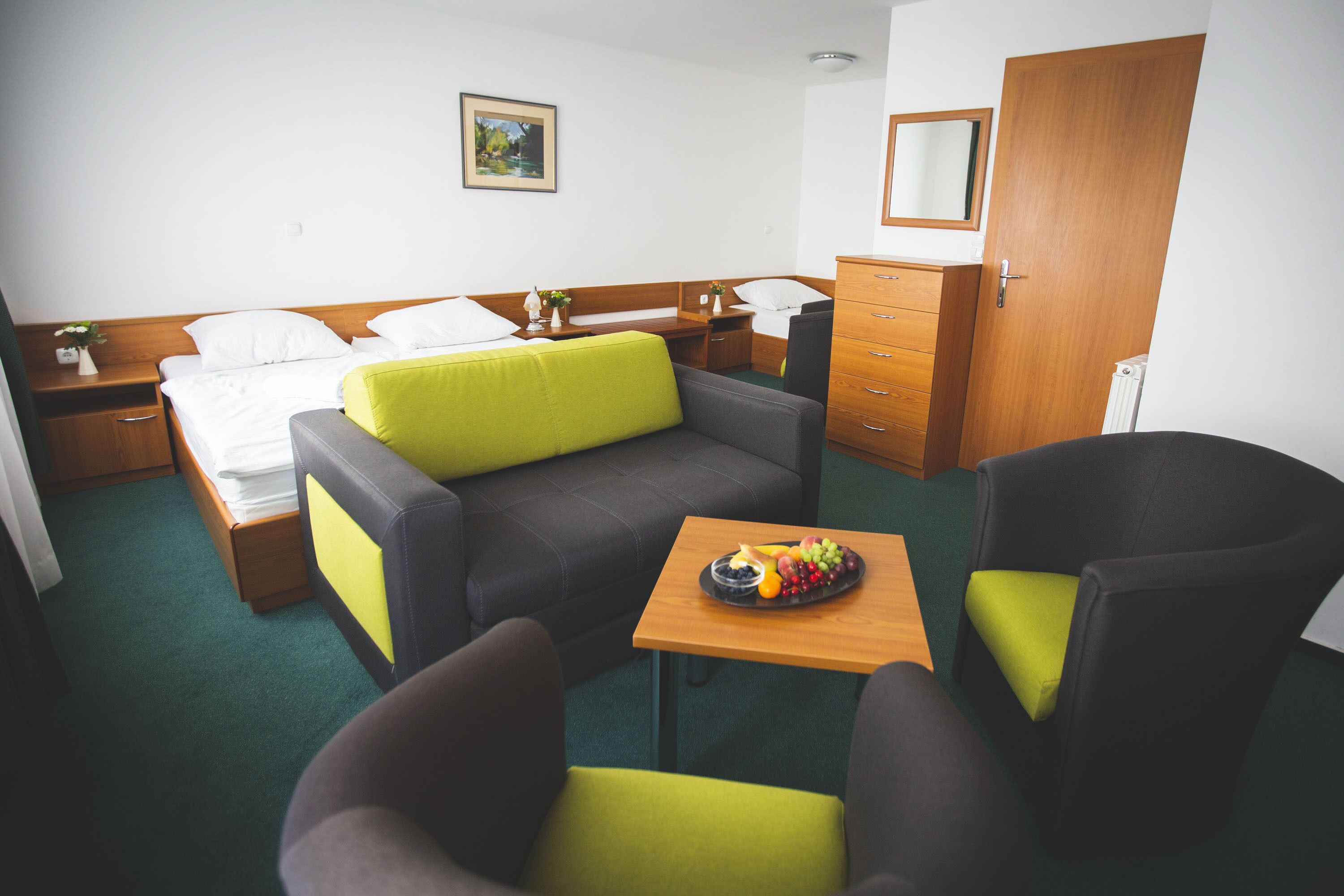 Une chambre d’hôtel avec un lit, un canapé, une petite table avec des fruits, une chaise, une commode et un tableau au mur.