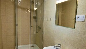Un baño con ducha de vidrio, lavamanos pedestal y espejo montado en la pared.