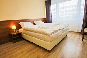 A double bed with a wooden headboard, a bedside table with a lamp, and a view of the outside through sheer curtains. - Sill Kielce (Kielce)