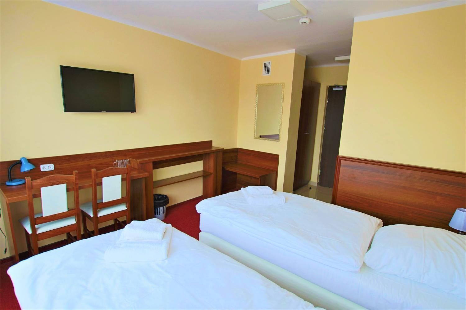 A hotel room with two beds, a desk, chairs, a TV, and a mirror.