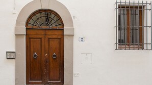 A double wooden door with a semi-circular arch above it, a small window with metal bars, and a wall-mounted electrical outlet. - Chiasso degli Armati Apartment (Florence)