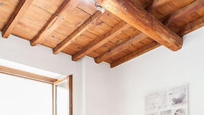 A bedroom with a wooden ceiling, a bed with white bedding and towels, a nightstand with a lamp, and a wall with a framed picture. - Chiasso degli Armati Apartment (Florence)