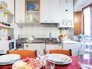 Cocina pequeña con armarios blancos, microondas, pileta y estufa. Hay una mesa de comedor con platos y un vaso de agua.