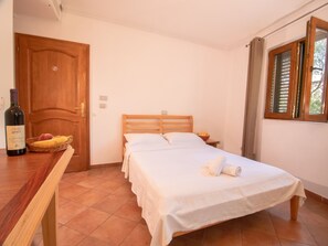 Een slaapkamer met een houten bed, een nachtkastje, een rieten mand met fruit en een fles wijn op een houten tafel.