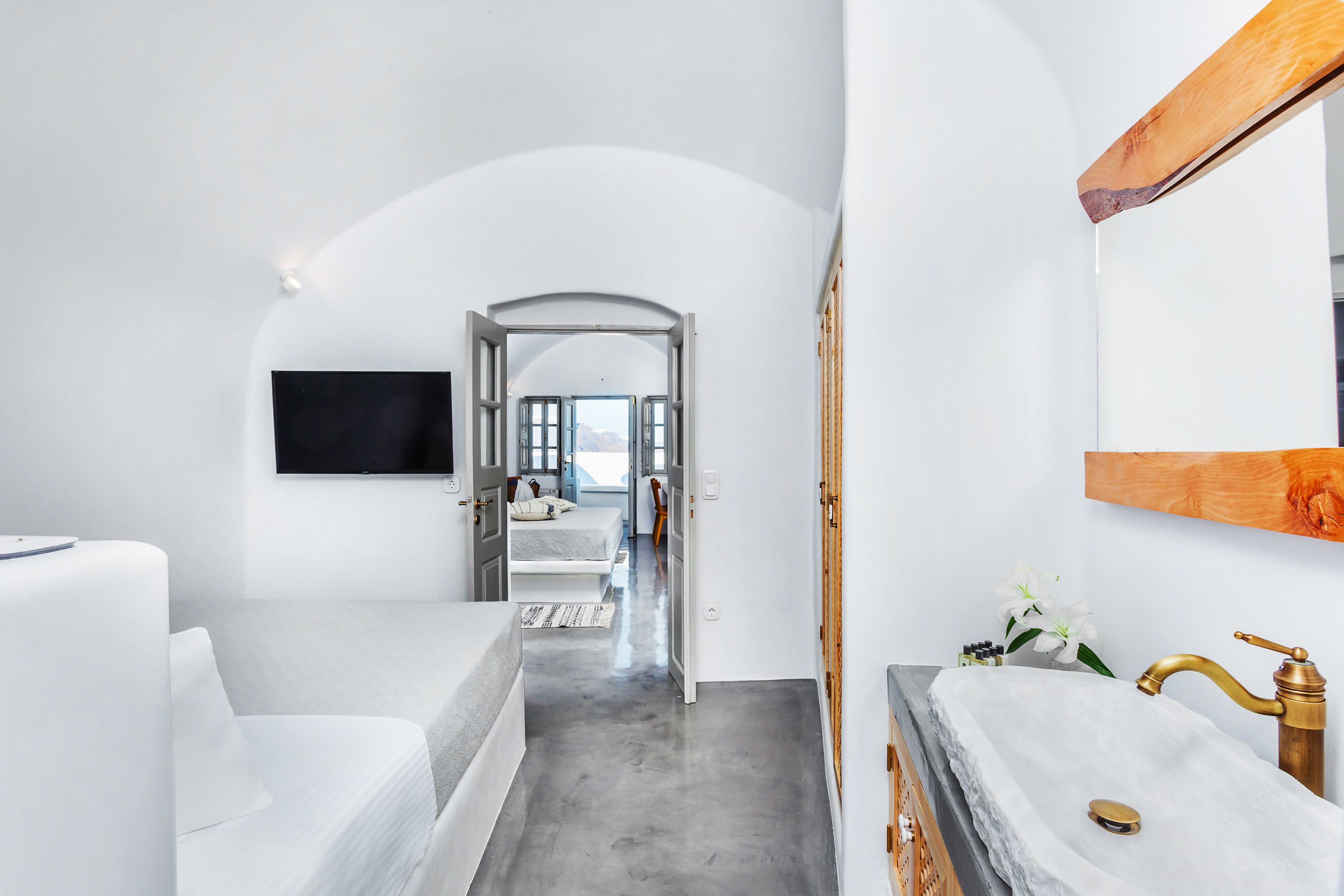 A modern bedroom with a large bed, a vanity with a marble countertop, and a TV mounted on the wall.