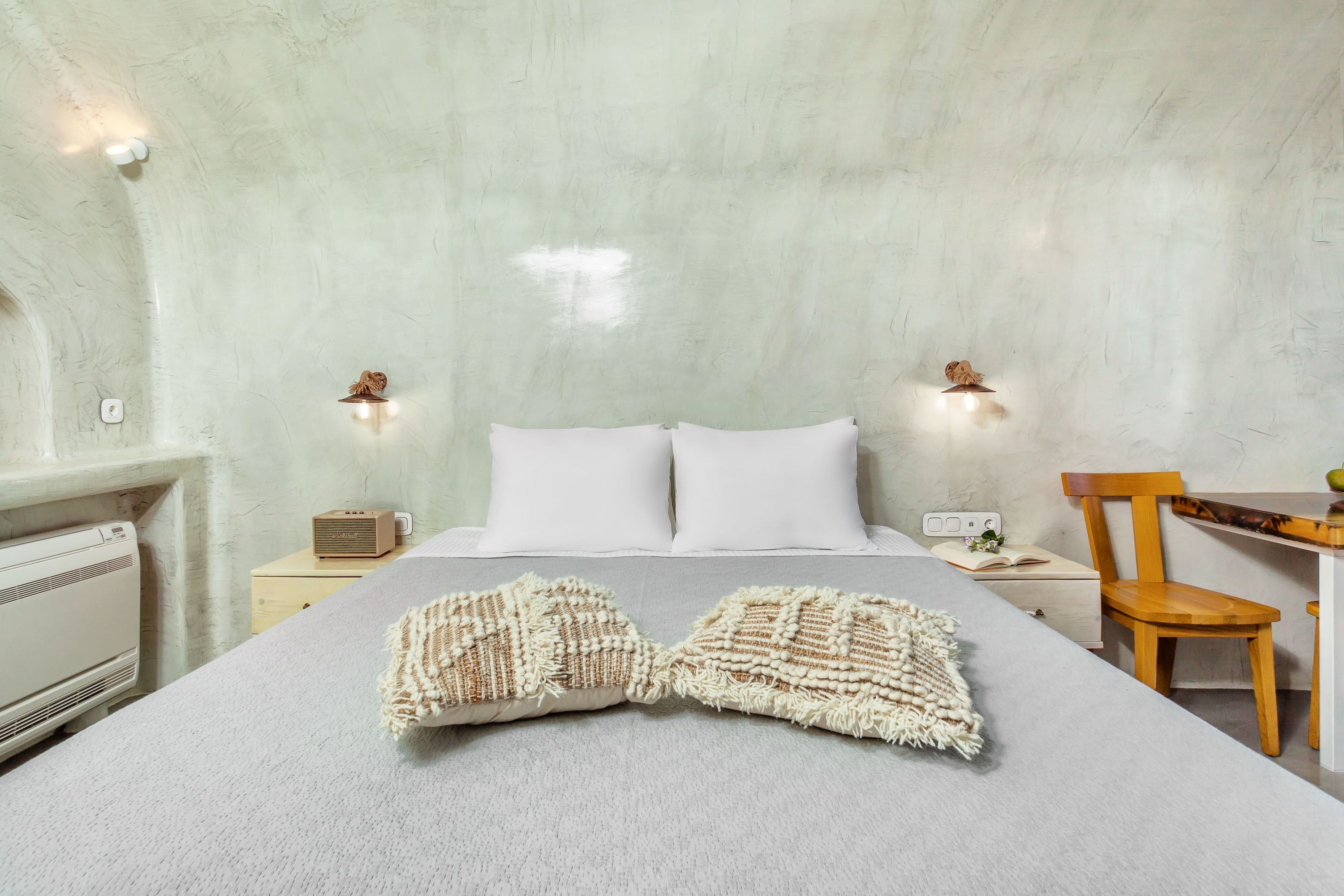 A bedroom with a bed, two bedside tables, a chair, and a small table with a plant.