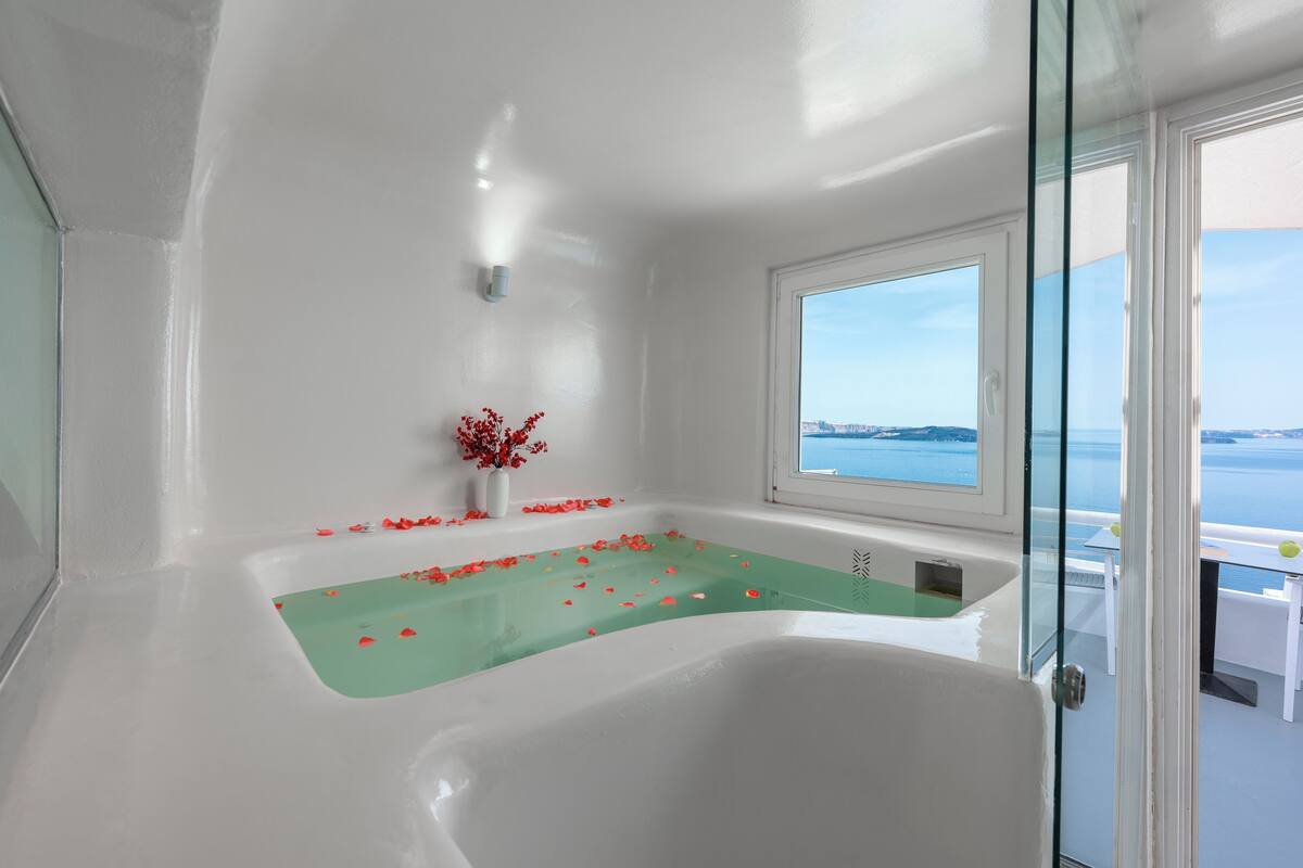 Ein modernes Badezimmer mit einer großzügigen Badewanne, einer Duschkabine aus Glas und Meerblick durch ein großes Fenster.