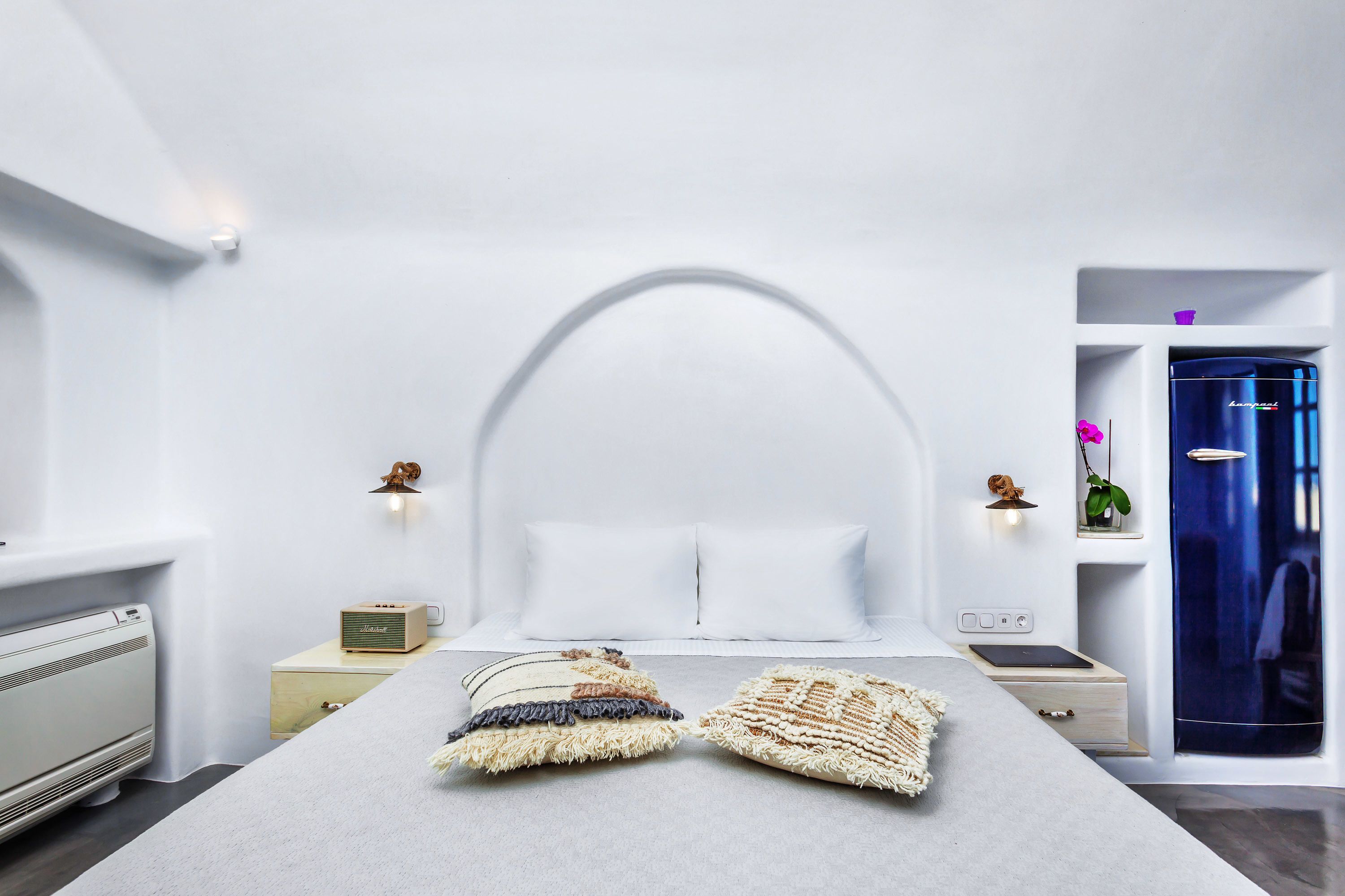 Un dormitorio moderno con una cama grande, una mesita de noche, un armario azul y un pequeño estante con adornos.