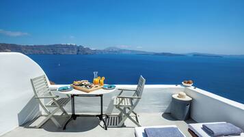 Een zonnig terras met een ontbijt tafel, met uitzicht op een heldere blauwe zee en verre kliffen.