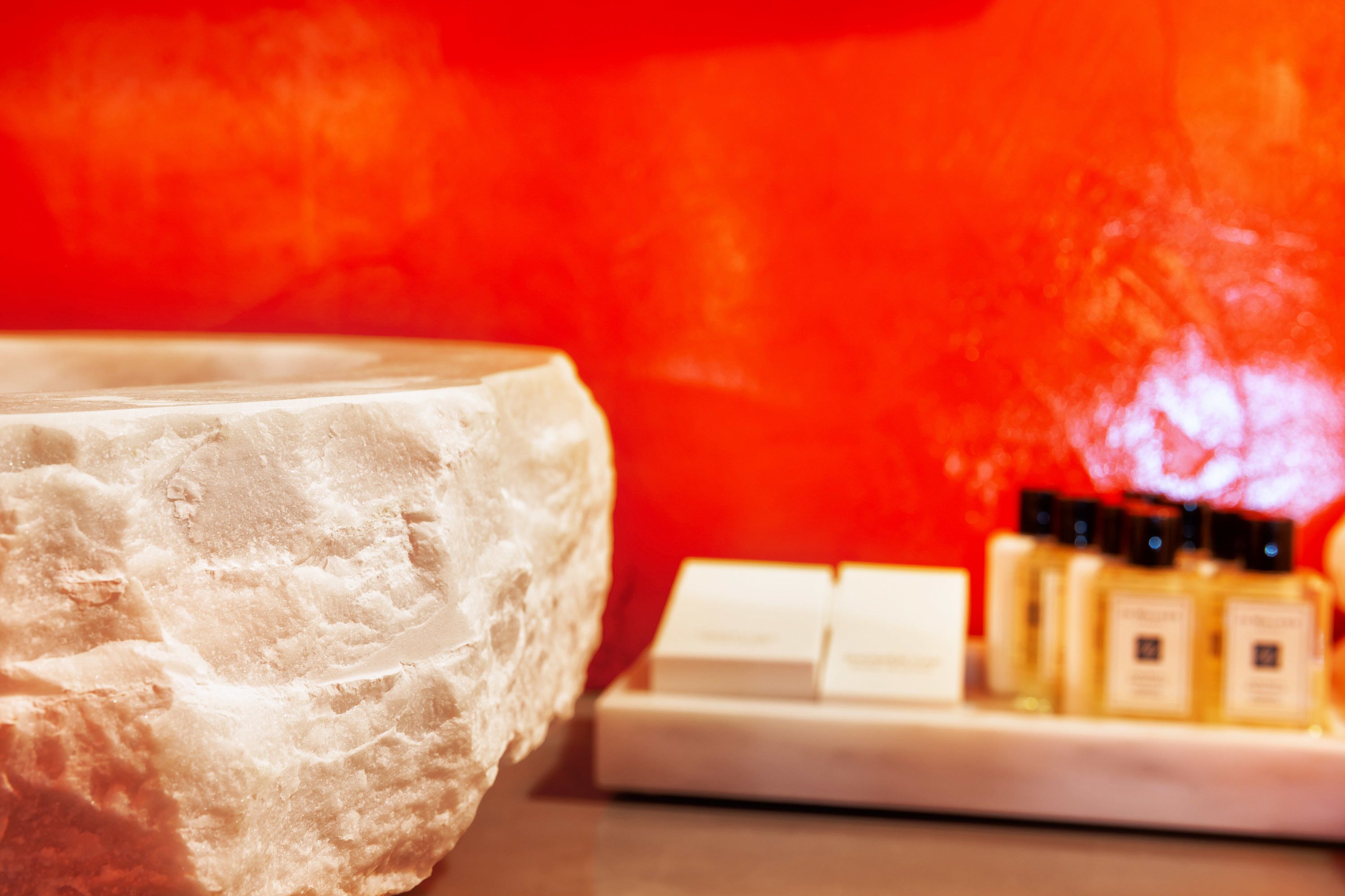 A stone basin with a white countertop and a row of perfume bottles.