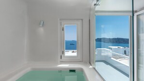 A modern bathroom with a large window, a bathtub, and a view of the sea and a boat. - Diamond Luxury Suites Collection (Santorini)