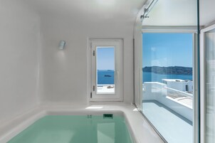 A modern bathroom with a large window, a bathtub, and a view of the sea and a boat.