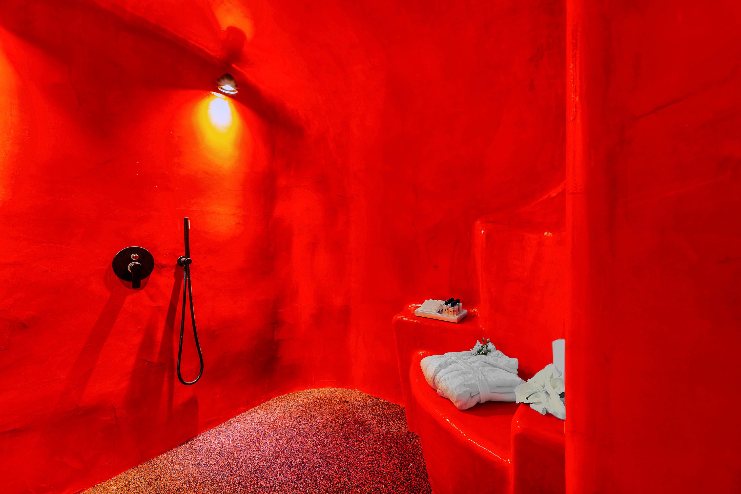 A red-walled room with a bench, a towel rack, and a small shelf with items.