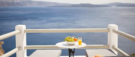 Un balcón con mesa lista para el desayuno, con vistas a un paisaje marino y terreno distante.