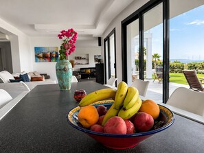 A modern living room with a dining table, a bowl of fruit, and a vase with flowers. - Villa Sophie Feet in the water! magnificent (L' Escala)