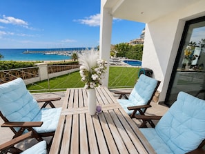 A balcony with a wooden table and four chairs, overlooking a pool and beach. - Villa Sophie Feet in the water! magnificent (L' Escala)