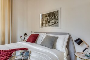A neatly made bed with white linens, a red throw blanket, and a framed black and white photo on the wall.