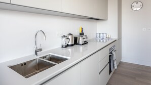 A modern kitchen with a stainless steel sink, a kettle, a toaster, and a clock on the wall.