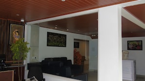 Un salon avec un canapé noir, une table basse et une plante en pot. Les murs sont ornés de tableaux et le plafond est en bois.