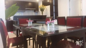 A modern kitchen with dark cabinetry, a glass dining table, and red upholstered chairs. - Hanoi A83 Hotel (Hanoi)
