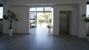 Un hall d’entrée spacieux au design moderne, doté d’une grande porte vitrée donnant sur un espace extérieur, d’un comptoir de réception et de plantes en pot.