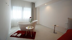 Une salle de bain moderne avec une baignoire sur pieds, une petite table ronde ornée d’un vase de fleurs et un tapis rouge sur le sol.