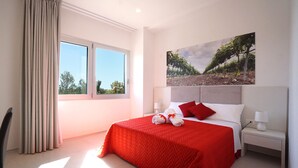 Une chambre d’hôtel avec un grand lit, une fenêtre avec des rideaux, une table de chevet avec une lampe et un tableau au mur.