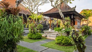 Um templo tradicional balinês com telhado de telhas, cercado por vegetação exuberante e um caminho de pedra.