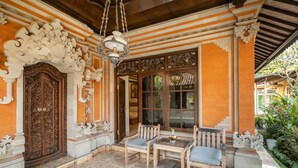 Uma entrada ornamentada com uma porta de madeira grande, um espaço de pátio com azulejos e móveis de madeira, e um lustre pendurado.