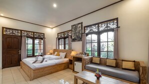 Quarto bem iluminado com cama de madeira, um sofá, uma mesinha e um objeto decorativo na parede.