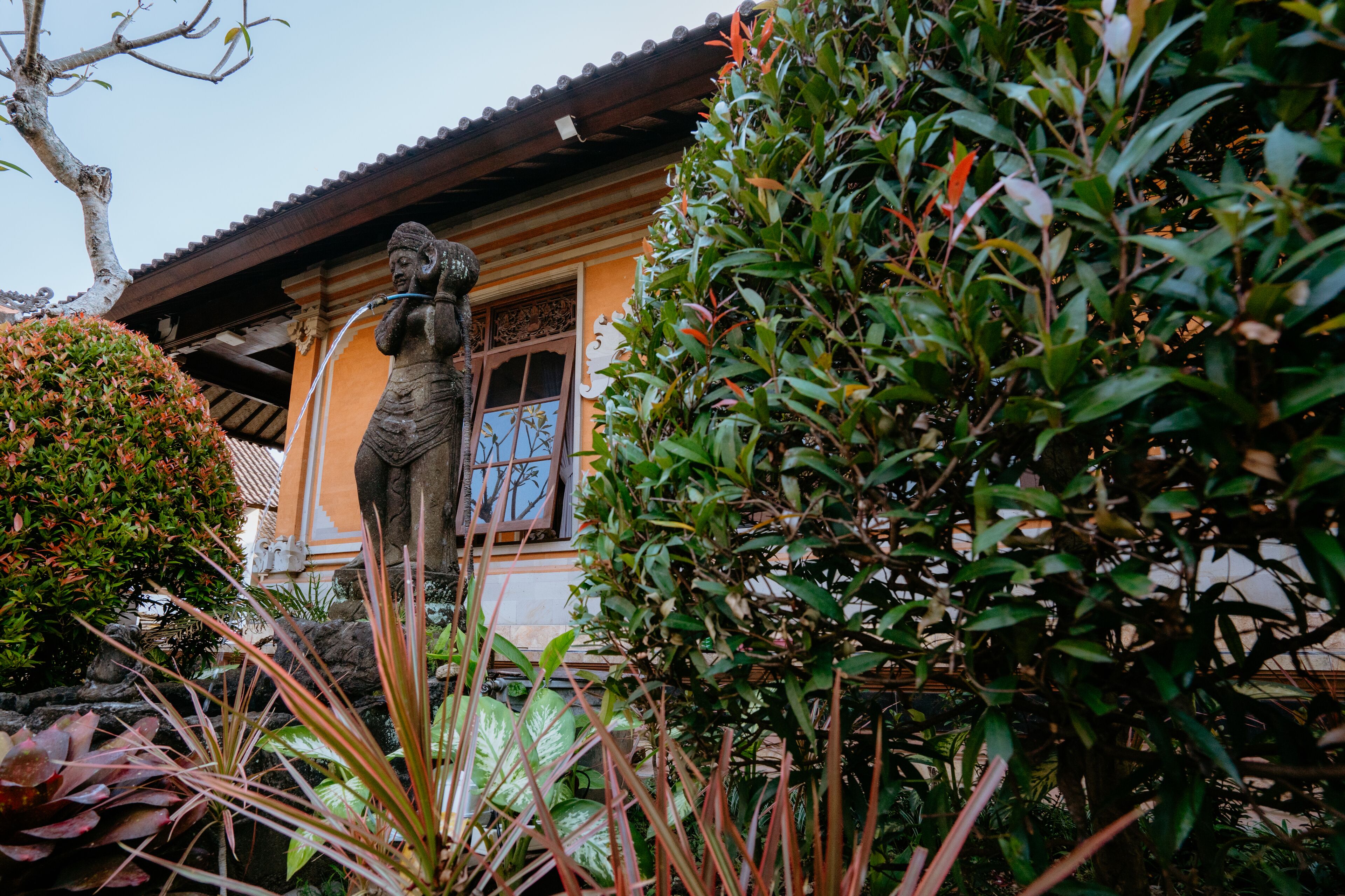 A traditional building with a tiled roof, a statue, and lush greenery.