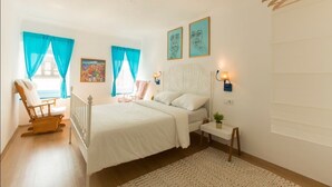 Un dormitorio con cama, una silla, una mesita de noche y un ventanal con cortinas.