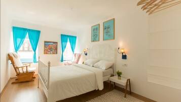 A bedroom with a bed, a chair, a bedside table, and a window with curtains.
