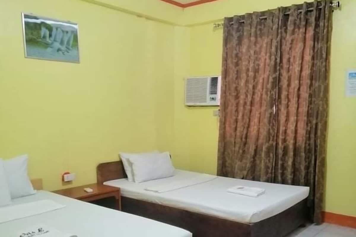 Ein Hotelzimmer mit zwei Einzelbetten, einem kleinen Tisch, einem Stuhl, einer Wandklimaanlage und einem Vorhang.