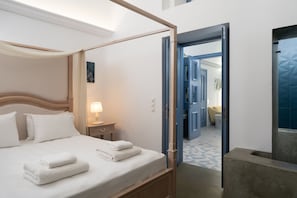 A hotel room with a four-poster bed, a bedside table with a lamp, and a view of the hallway. - Bliss Mansion (Santorini)