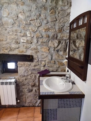 A bathroom with a stone wall, a white sink, a mirror, and a tiled floor.