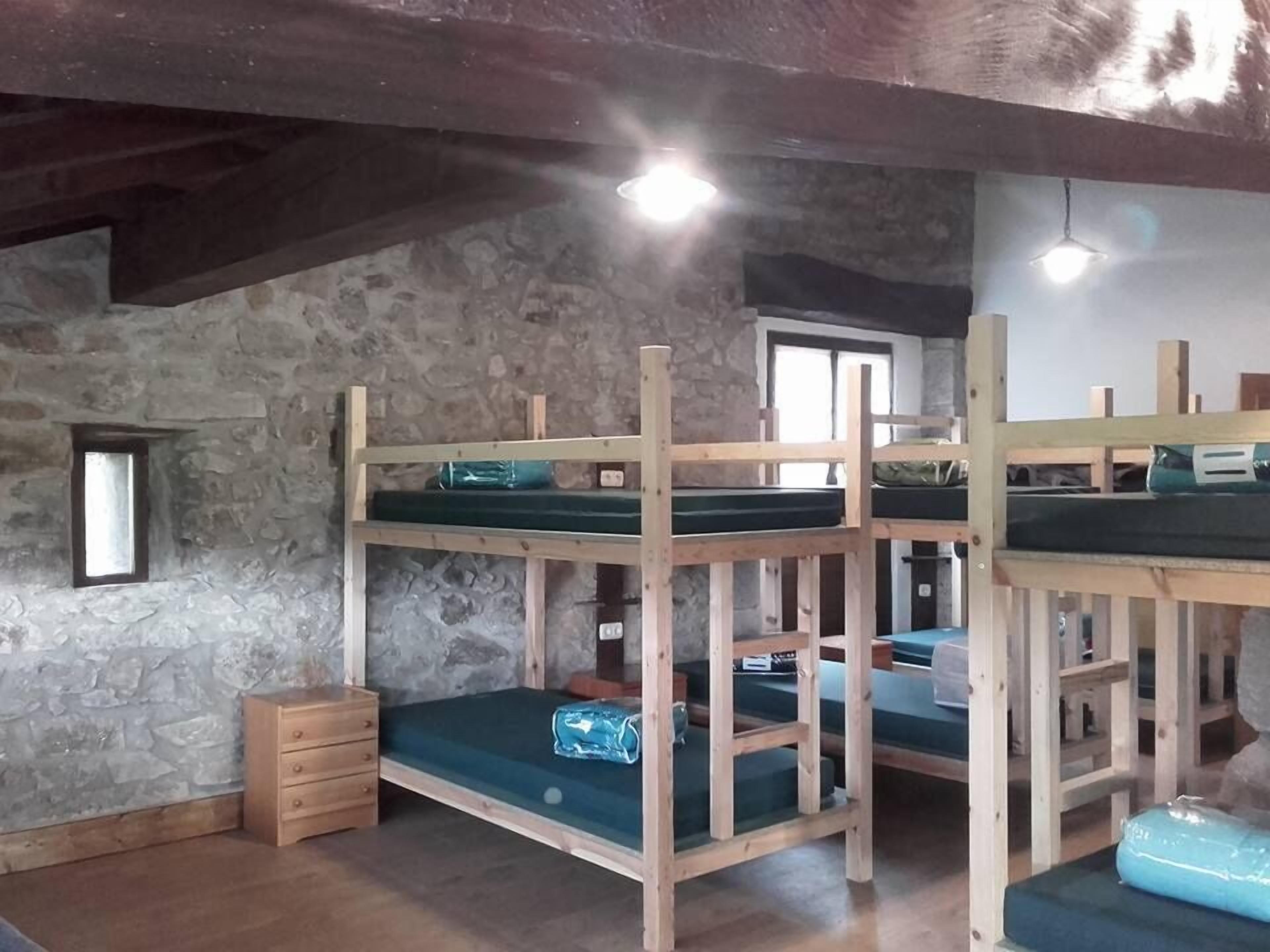 A rustic room with bunk beds, a stone wall, a small window, and a wooden dresser.