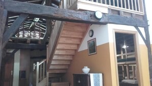 Een meerlaags houten constructie met een trap, een klein tafeltje met een kom, en een deur die naar een andere kamer leidt.