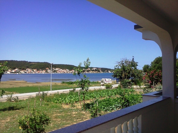 A balcony with a view of a coastal area, including a road, greenery, and a body of water. - Apartments and Rooms Viskic (Rab)