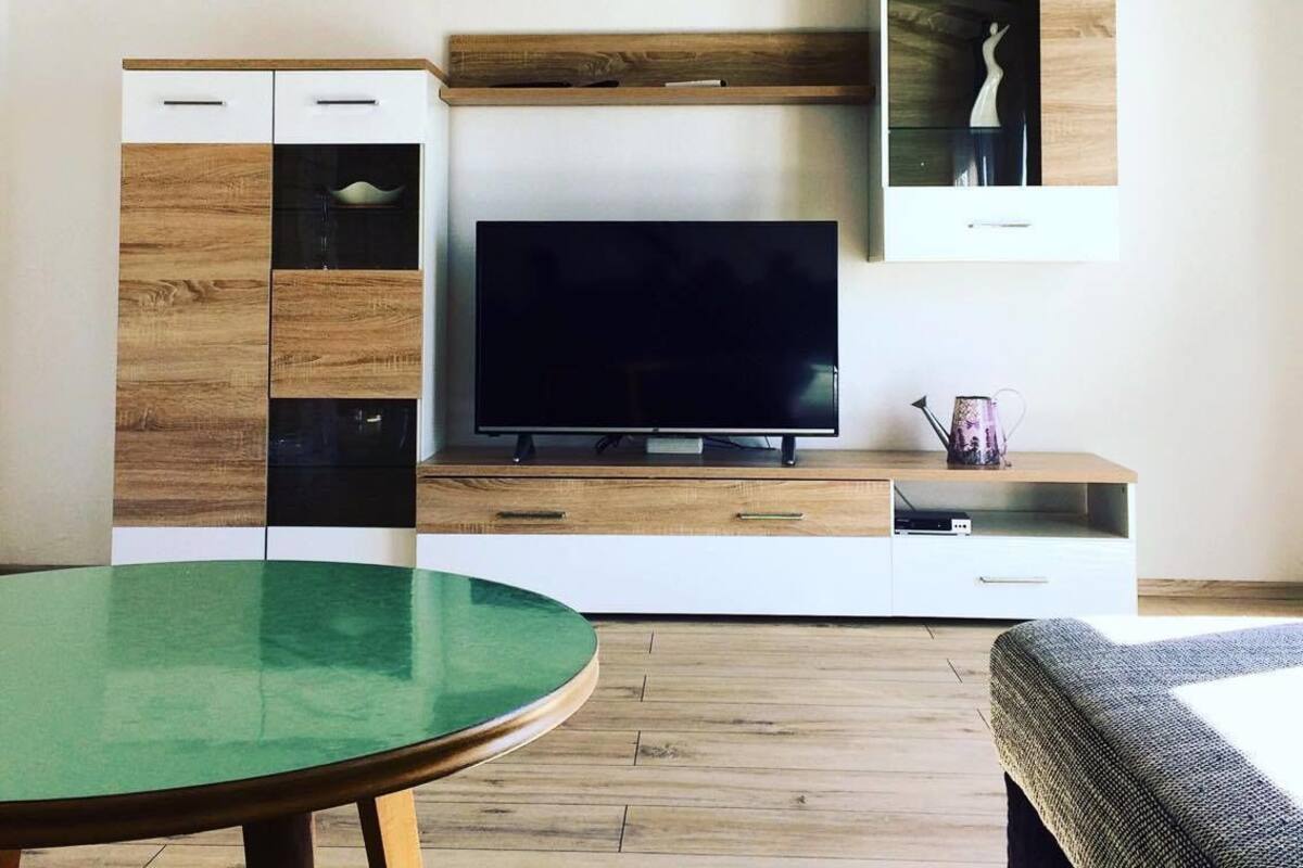 A modern living room with a flat-screen TV, wooden cabinets, a glass coffee table, and a sofa.