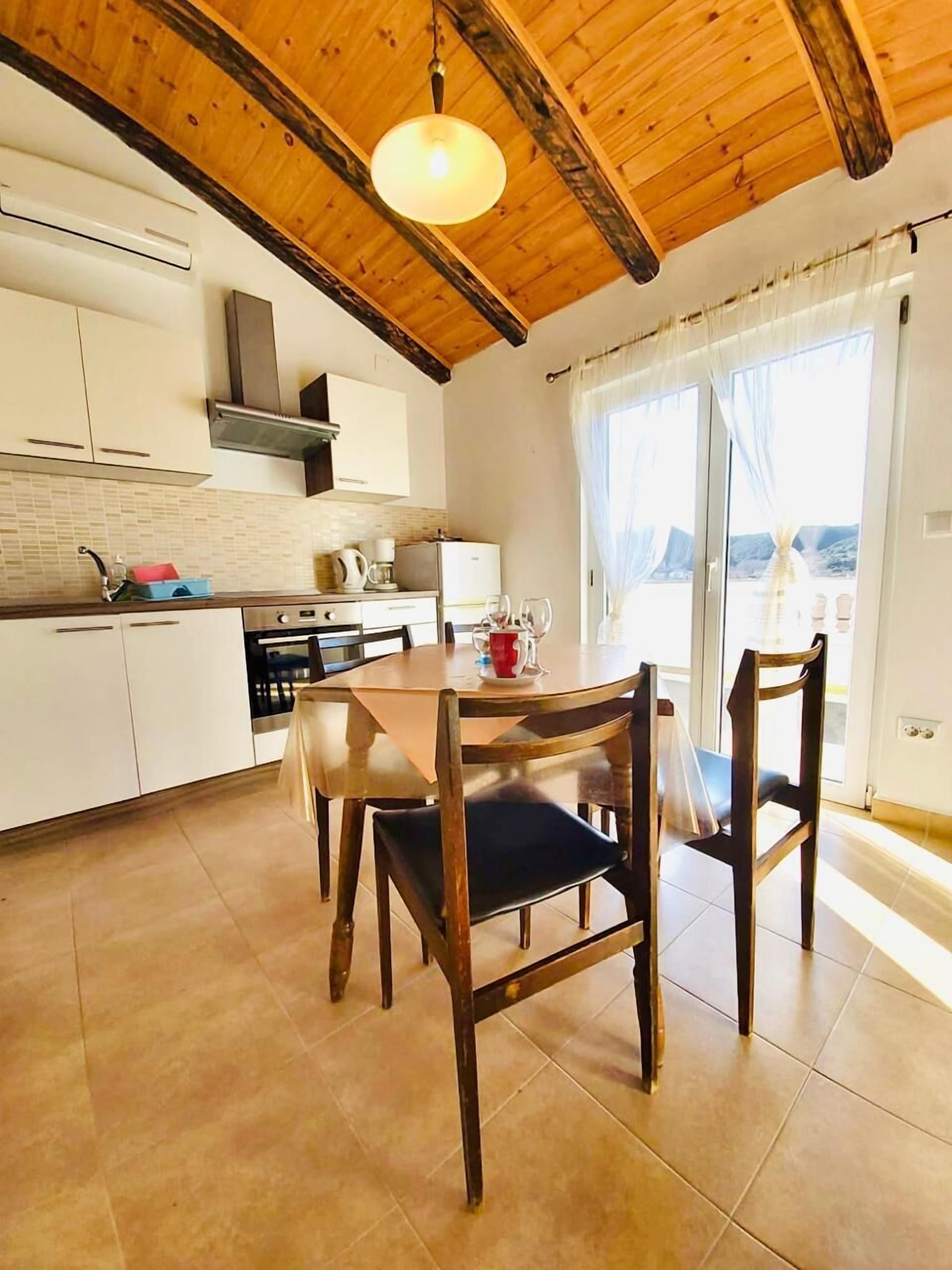 Une cuisine avec des poutres en bois, une table à manger avec des chaises et une vue par la fenêtre.
