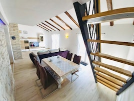Un comedor con mesa y sillas, una cocina al fondo y una escalera con barandillas de madera.